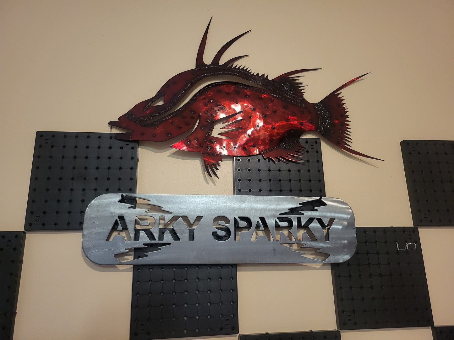 Decorative metal fish sculpture with 'ARKY SPARKY' sign on a checkered background